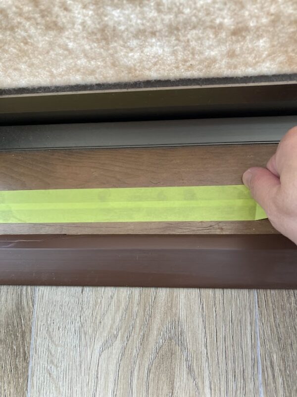 二重窓のレール幅に合わせて、マスキングテープを2列並べて貼り、下地を広めに保護している様子。