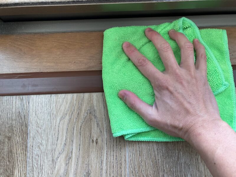 二重窓のレールを貼り付ける前に、窓枠の汚れを雑巾で綺麗に拭き取っている様子。