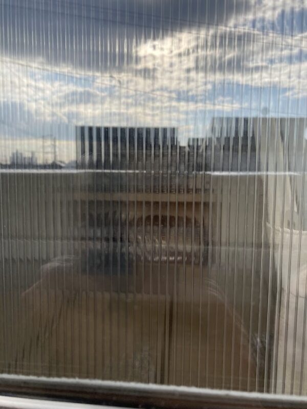 ポリカーボネート製の二重窓越しに見える外の景色。縦のラインによって視界が適度に遮られ、プライバシー保護（目隠し）効果があることを示している。