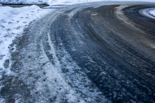 濡れた路面のように見えるが、表面が薄く凍りついたブラックアイスバーンのカーブ