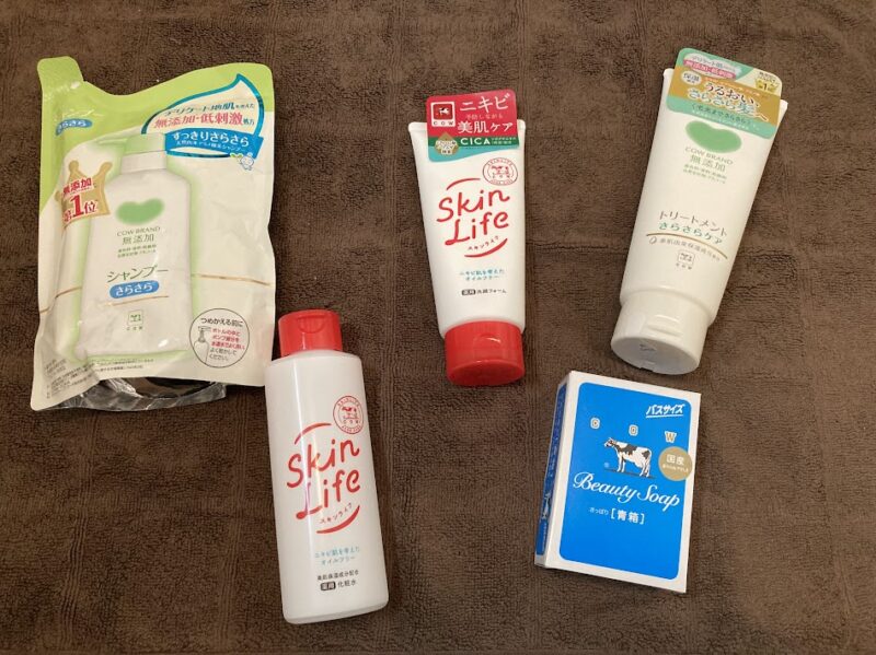 バスタオルの上に並べられた牛乳石鹸カウブランドのフルセット（シャンプー、洗顔、化粧水、石鹸、トリートメント）。