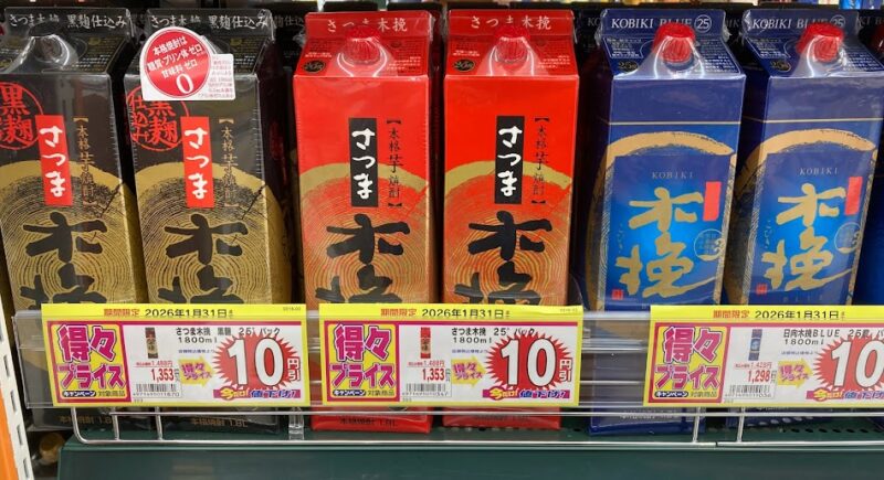 ドラッグストアモリのお酒売り場に並ぶ「さつま木挽 赤」の1.8Lパック。隣には定番の黒麹仕込みや木挽BLUE（青）も並んでおり、期間限定の「得々プライス」1,353円で販売されている様子。