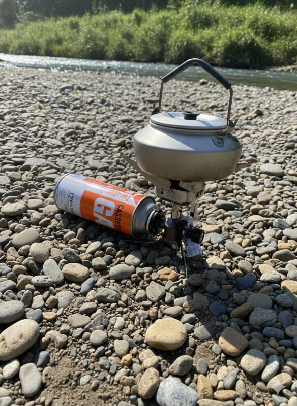河原の石の上でイワタニのジュニアコンパクトバーナーにアルミケトルを載せてお湯を沸かしている様子