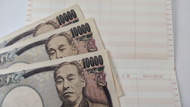 銀行通帳と日本円の札束。サラリーマンが毎月手にすることができる「安定した給与収入」と、それゆえに泥船から抜け出せない葛藤を象徴するイメージ画像。