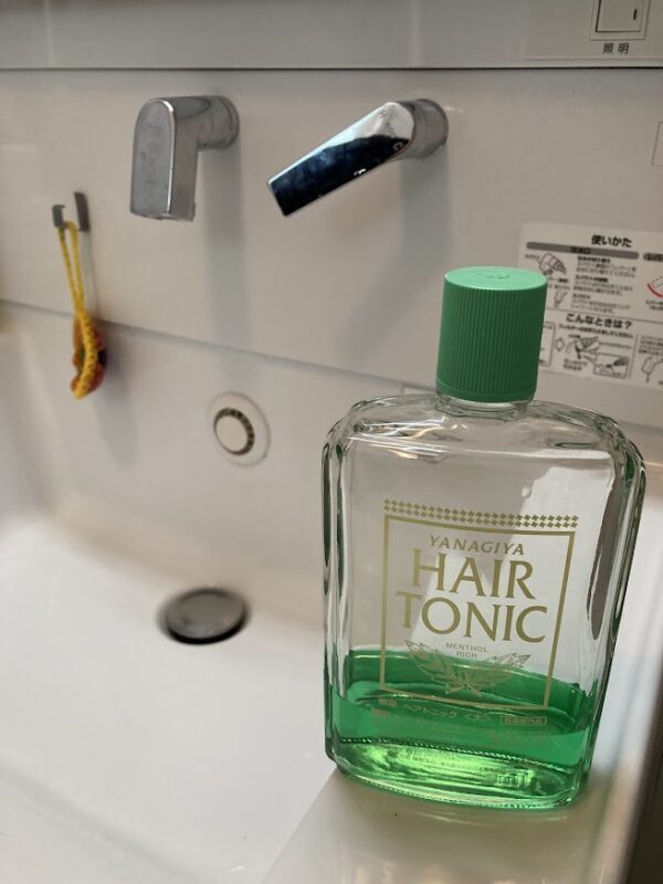 洗面台の縁に置かれた柳屋ヘアトニックのボトル。爽やかなグリーンの液体とガラス瓶の清潔感。