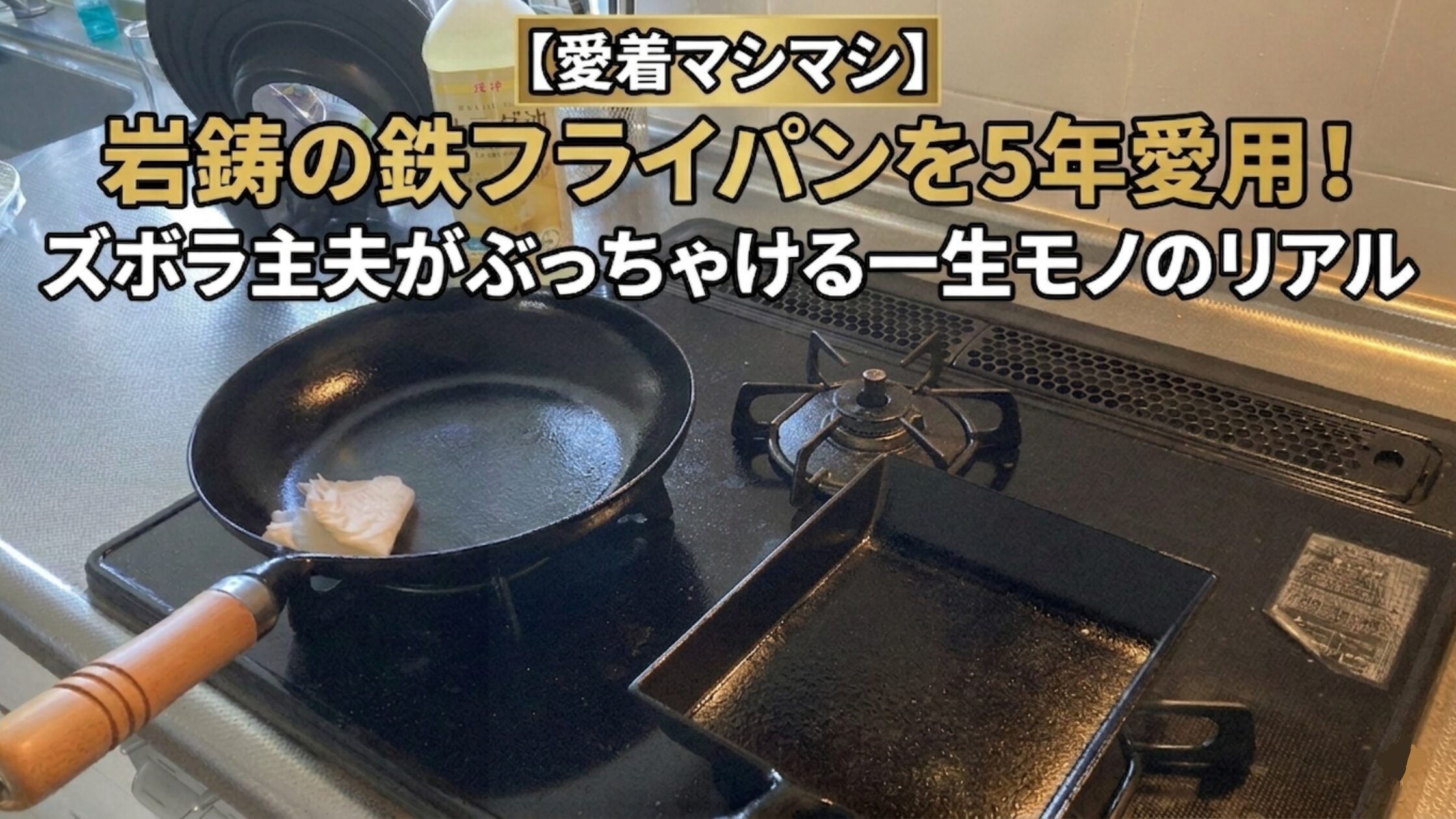 キッチンカウンターのガスコンロの上に、岩鋳の南部鉄器フライパンと、同じく南部鉄器の卵焼き器が並んで置かれている。フライパンにはキッチンペーパーが敷かれており、どちらも使い込まれた様子がうかがえる。背景には油の瓶やキッチン用具が見える。