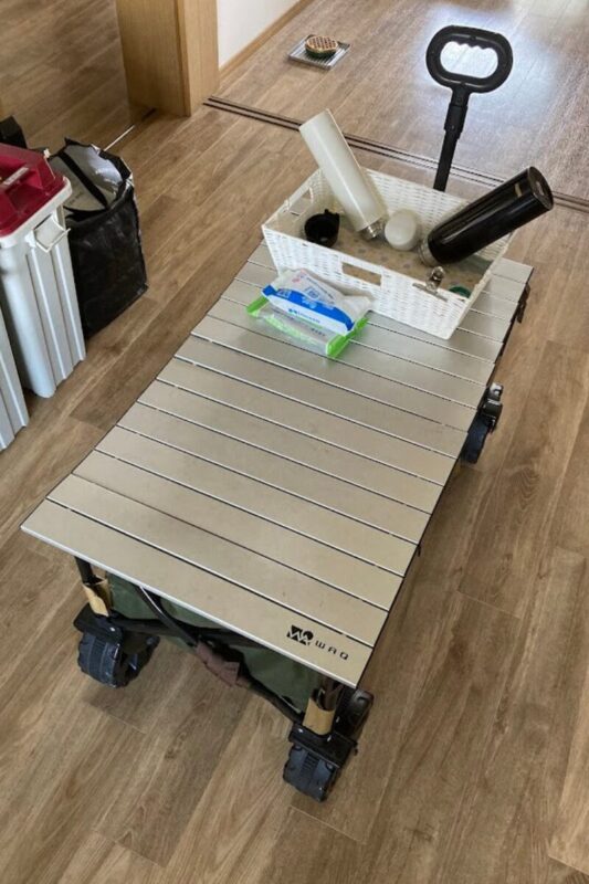 WAQアウトドアワゴンをキッチンで作業台として活用し、アルミテーブルの上に水筒や小物を置いている様子