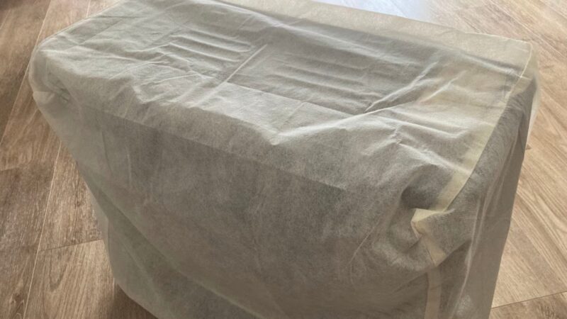 100円ショップで購入した不織布製のファンヒーター(ストーブ)用ほこり除けカバーを本体にかぶせている使用写真。全体がすっぽりと覆われて保管されている様子。