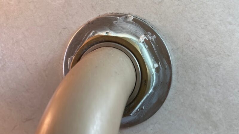 浴室の壁に設置されたシャワーバーの根元が、白いシリコンまたはボンドで固く固定されている様子
