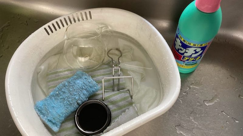 キッチンシンクの洗い桶で、キッチンブリーチを使って台拭きやコップ、スポンジ置きなどをまとめて漂白している様子